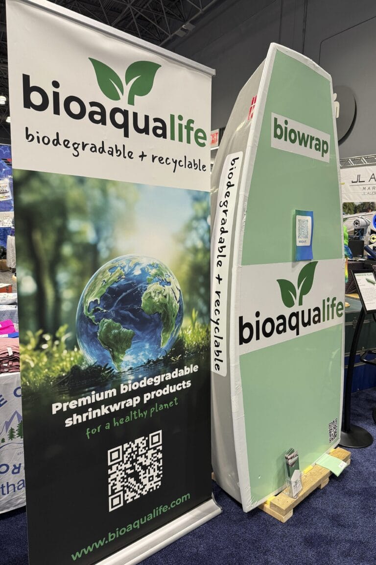 bioaqualife: A trade show booth for bioaqualife featuring a green and white surfboard-shaped display and a banner. The banner promotes biodegradable and recyclable shrink wrap products, with an image of Earth, a QR code, and the Bioaqualife website URL.