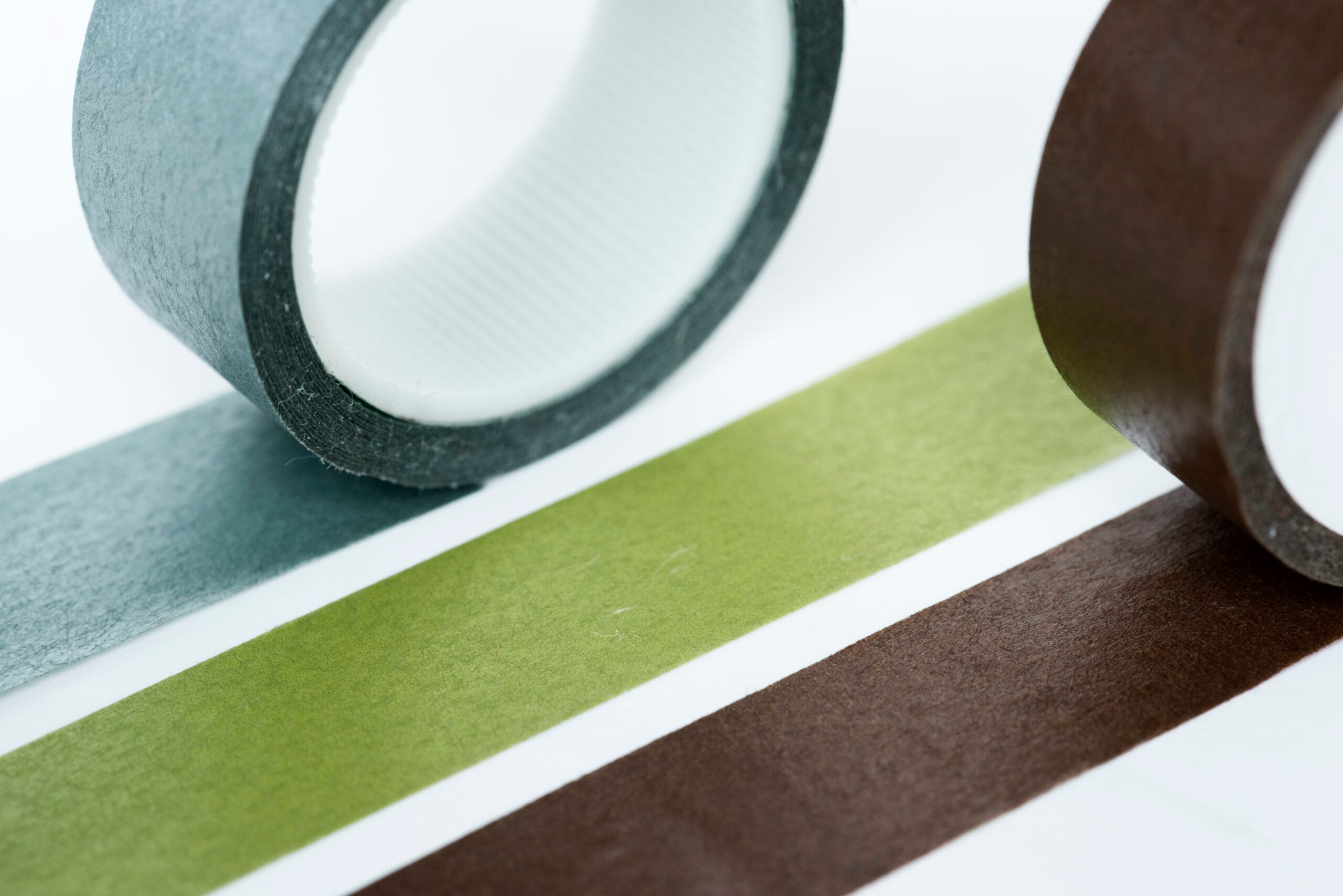 bioaqualife: Close-up of three rolls of adhesive tape in gray, green, and brown, each next to a matching strip of tape laid out flat on a white surface.