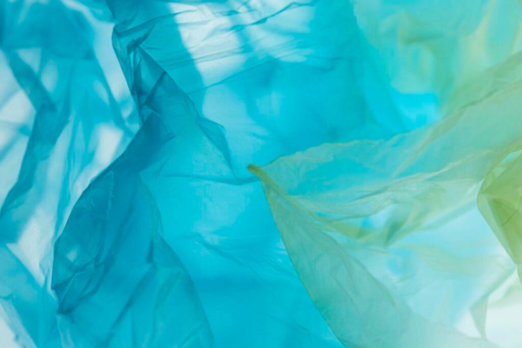 bioaqualife: A close-up of translucent blue and green plastic sheets layered together, creating a soft, flowing pattern with gentle lighting casting shadows and highlights.