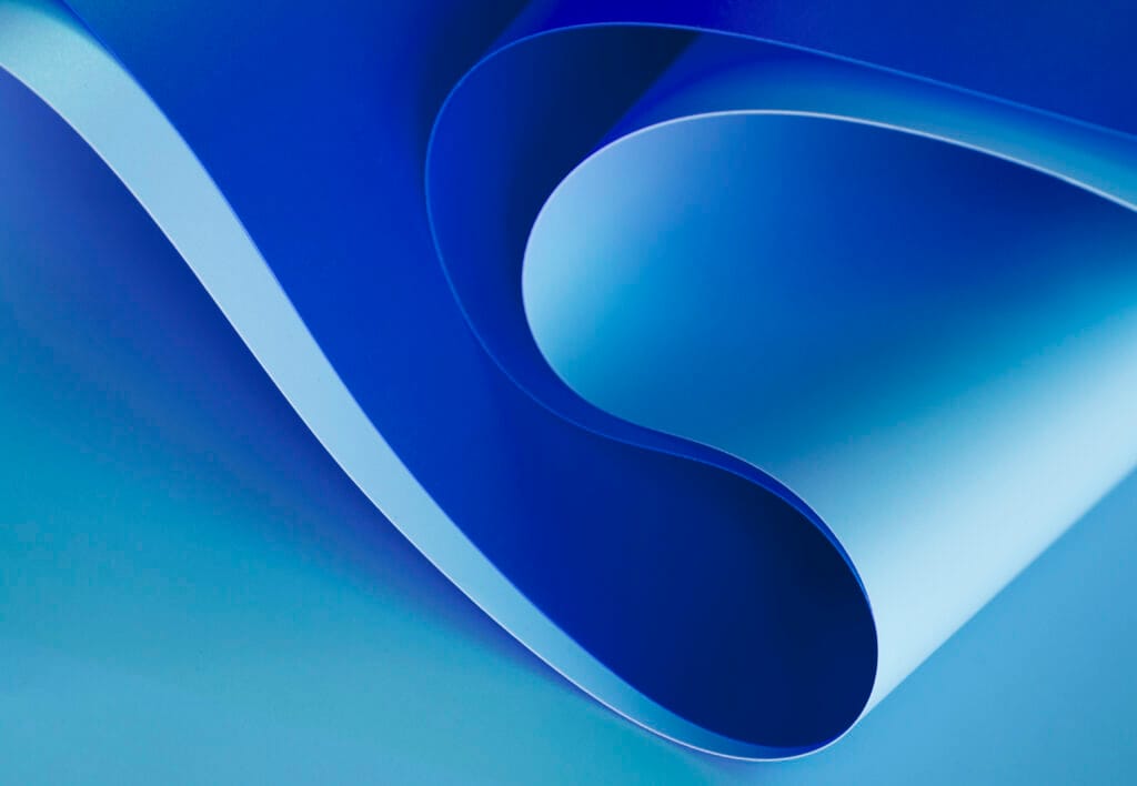 bioaqualife: A close-up of a curved, overlapping blue paper creating an abstract, wave-like pattern. The lighting highlights the paper's smooth texture, with varying shades of blue and soft shadows enhancing the depth and fluidity of the composition.