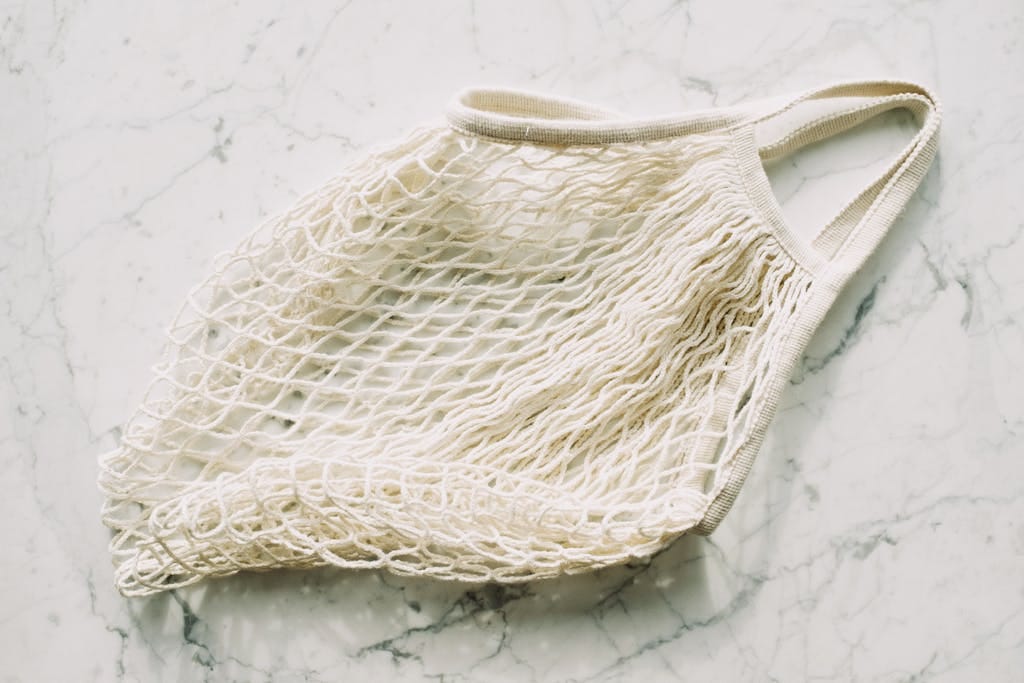Top view of simple eco friendly white mesh bag arranged on marble surface in room