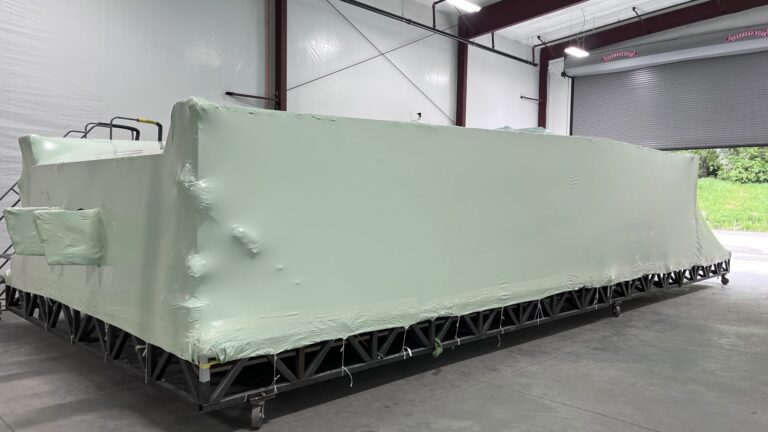 bioaqualife: A large, rectangular object wrapped in light green protective plastic sits on a metal frame inside a spacious industrial warehouse with high ceilings and an open garage door.