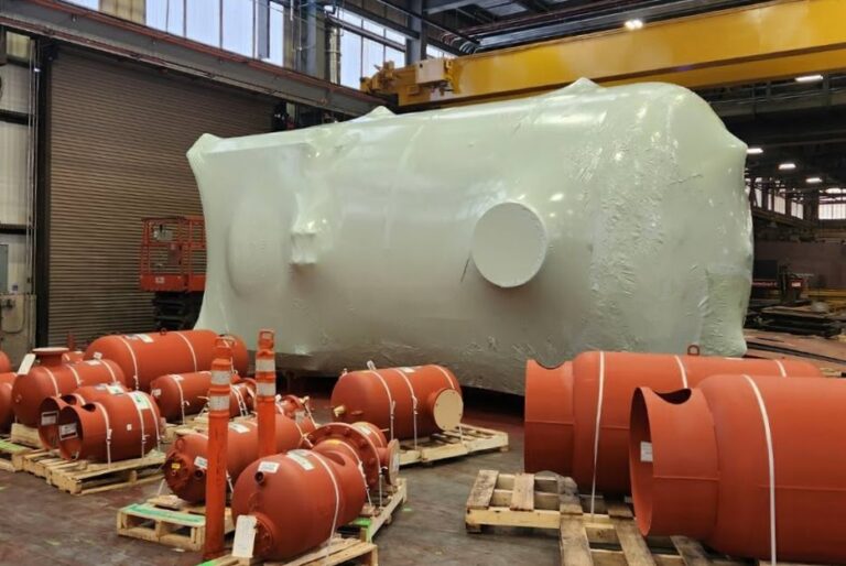 bioaqualife: Large industrial tank wrapped in white protective material next to several smaller red cylindrical tanks and equipment, all placed on wooden pallets inside a spacious warehouse with high ceilings.
