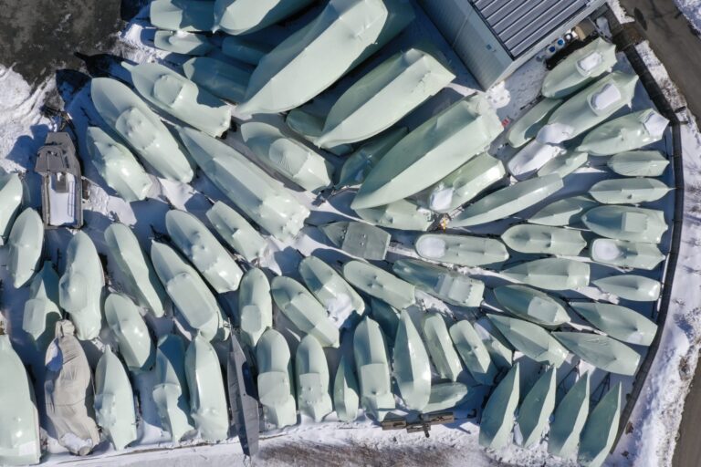 bioaqualife: Aerial view of numerous boats covered in protective wraps and arranged closely together in a snow-covered outdoor storage area near a building.